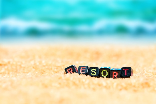 Multicolored word RESORT from black cubes in the sand on the background of beach and sea