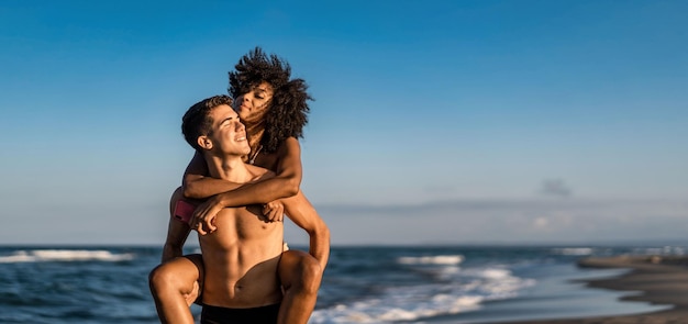 Multicultural couple of young lovers piggybacking on the beach