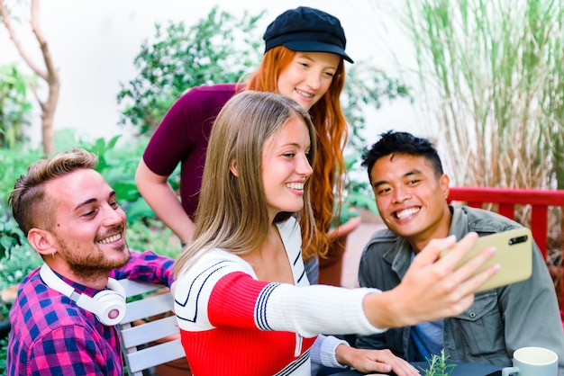 Multicultural group of happy young friends taking a selfie together on a mobile phone laughing and smiling as they pose as a group outdoors