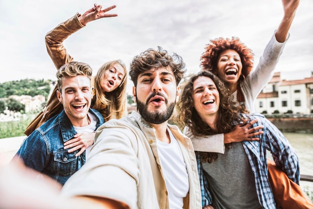 Multicultural happy friends having fun taking group selfie portrait on city street - Young diverse people celebrating laughing together outdoors - Happy lifestyle concept