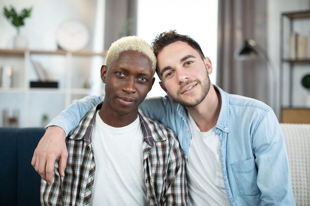 Multicultural same sex couple hugging and smiling on couch