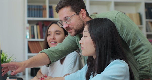 Multicultural students study for exams as a team use computer talk look for solution explain subject College students work together