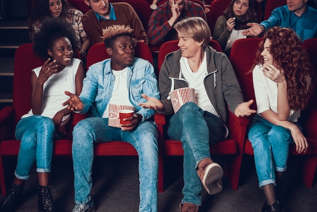 Multiethnic company of friends eating popcorn in cinema.