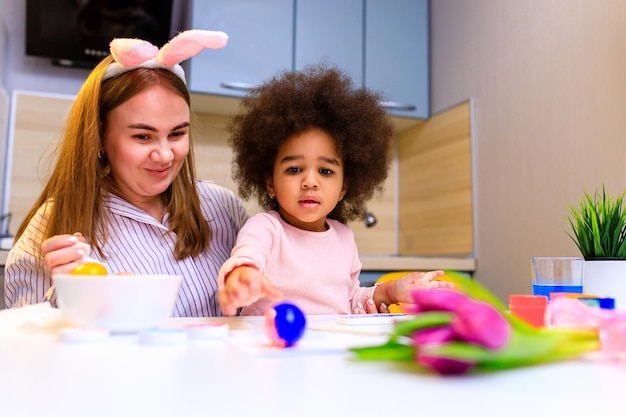 Multiethnic family preparing to easter event at kitchen painting eggs