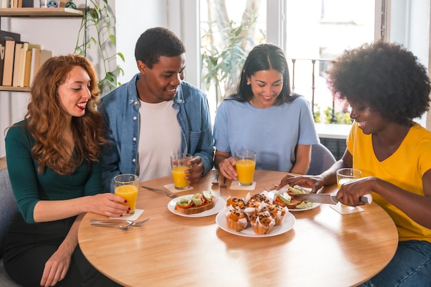 Multiethnic friends at a breakfast with orange juice and muffins at home cutting the toasts