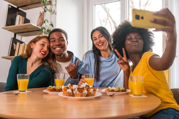 Multiethnic friends at a breakfast with orange juice and muffins at home selfie smiling