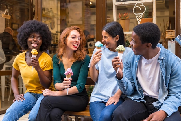 Multiethnic friends in an ice cream parlor sitting eating an ice cream laughing a lot