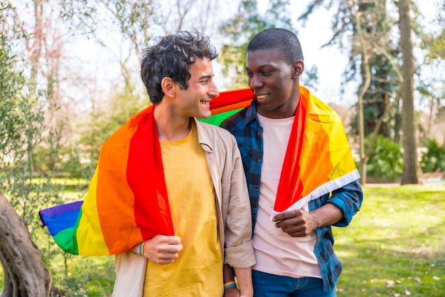 Multiethnic gay male couple holding a rainbow lgbt symbol flag having fun