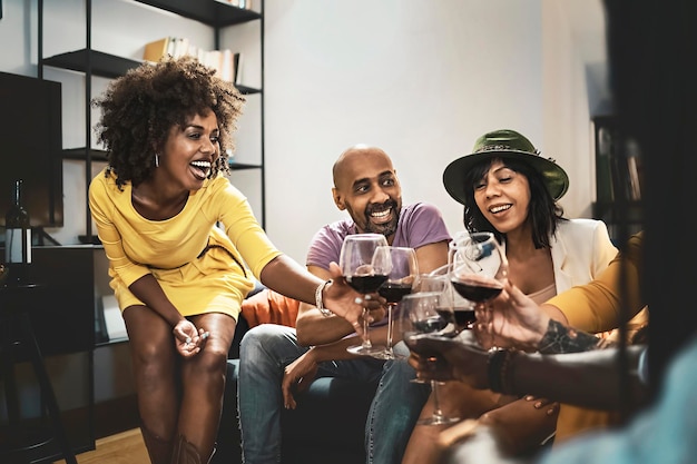 Multiethnic group of adult friends having fun toasting with red wine sitting on the sofa indoors