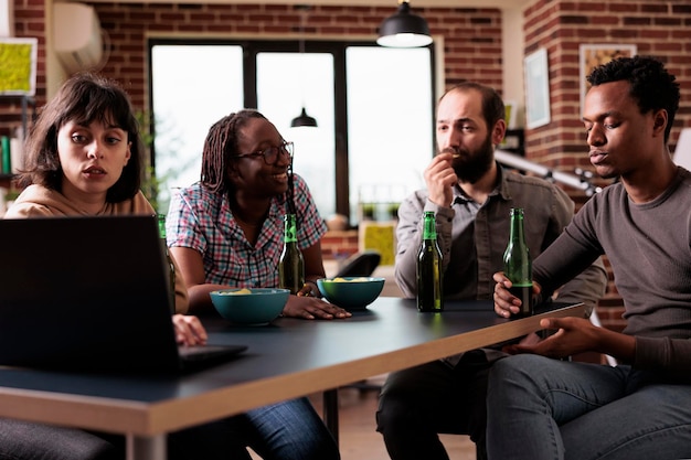 Multiethnic group of friends sitting at home together while watching drama movies on laptop computer. Diverse people sitting at table in living room while enjoying leisure activity.