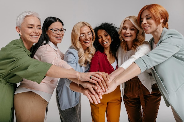 Photo multiethnic group of happy mature women holding hands together against grey background