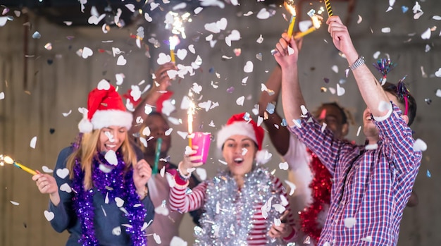 multiethnic group of young happy casual business people dancing and having confetti party while celebrating new year eve in front of concrete wall at new startup office