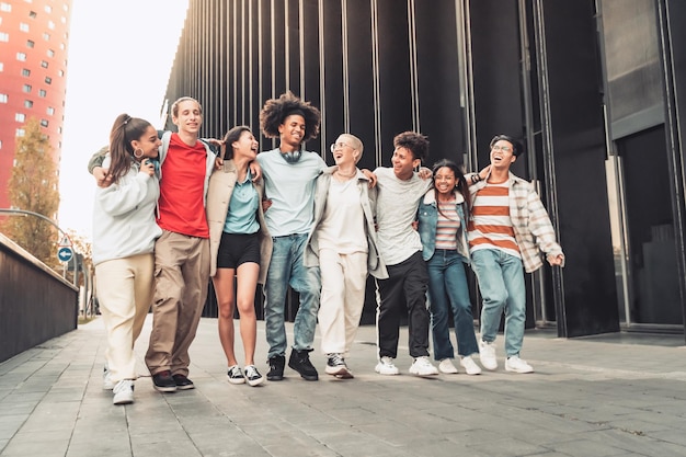 Multiethnic group of young happy friends walking down the street holding each other affectionately