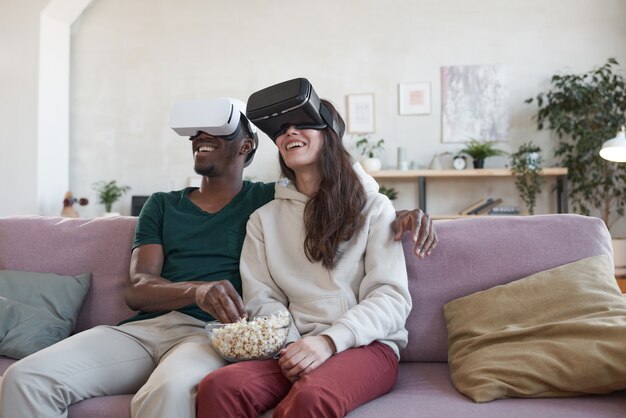 Multiethnic young couple eating popcorn while sitting on sofa and watching movie online at home