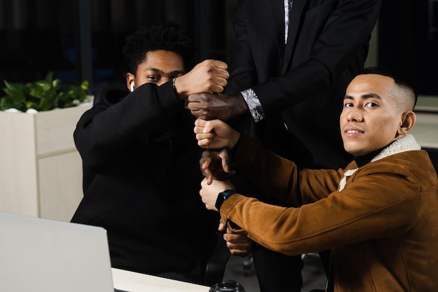 Multiethnical diverse colleagues making hand stack of fists Black africans and asian working online with laptop in office