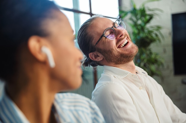 multinational joyful colleagues with earphones talking and laughing while working in office