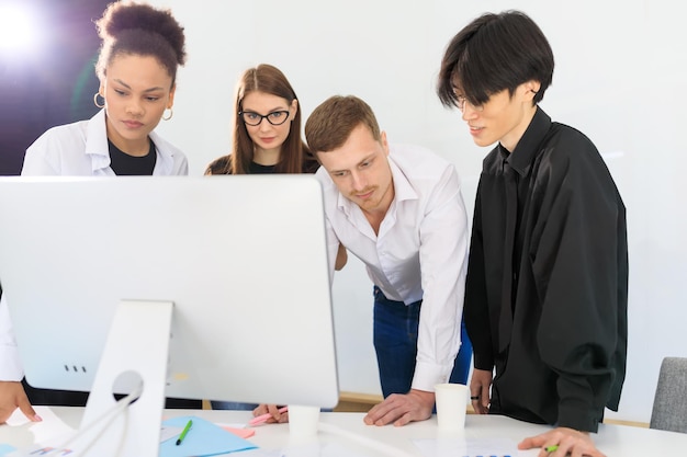 A multinational team stands in front of a computer in the office