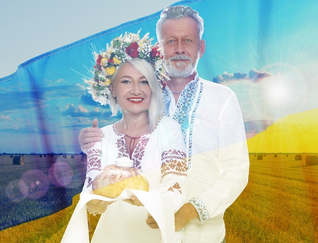 Multiple exposure of happy mature couple wearing national clothes with bread and salt wheat field and Ukrainian flag