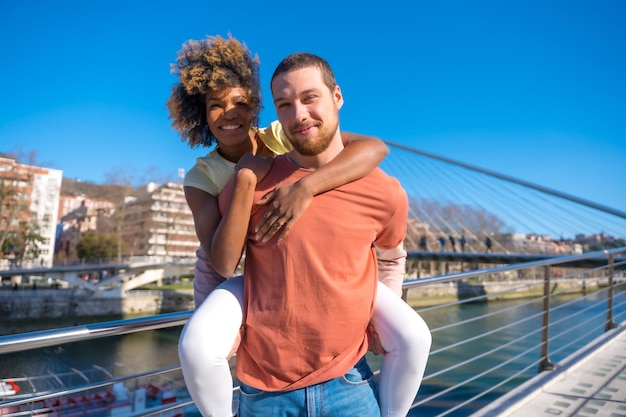 Multiracial couple on city street lifestyle smiling with girlfriend on back on catwalk