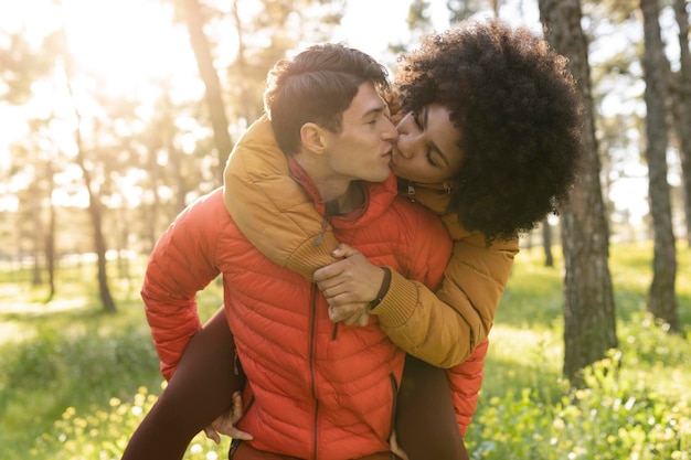 Multiracial couple outdoors Caucasian guy giving a piggyback ride to an African girl in the forest Concept of tourism friendship youth and weekend activities