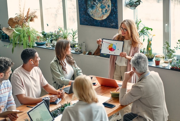 Multiracial creative people in modern office. Group of young business people and senior boss are working together with laptop, tablet, smart phone, notebook, graphs. Successful team in coworking