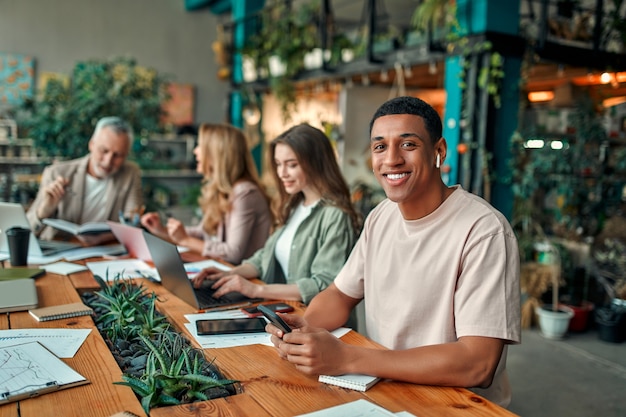 Multiracial creative people in modern office. Group of young business people and senior boss are working together with laptop, tablet, smart phone, notebook, graphs. Successful team in coworking