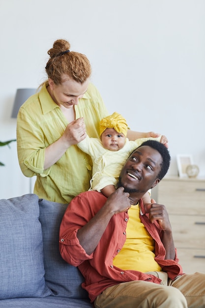 Multiracial family playing with their baby girl on the sofa at home