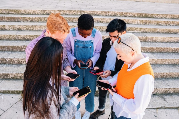 Multiracial friends chatting and browsing with smartphones in a group