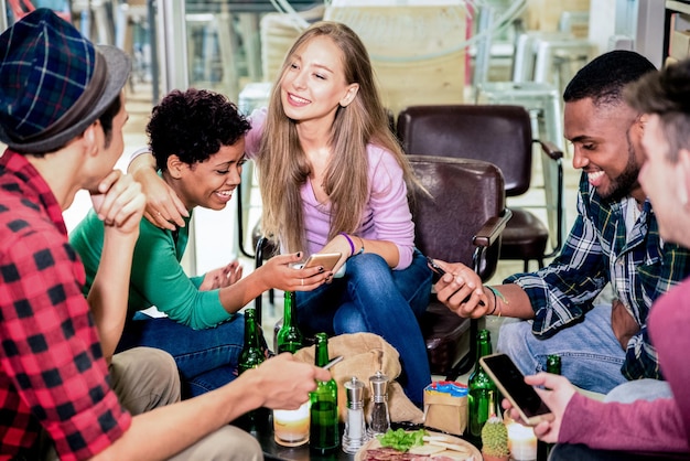 Multiracial friends group drinking beer and having fun with phones at cocktail bar restaurant