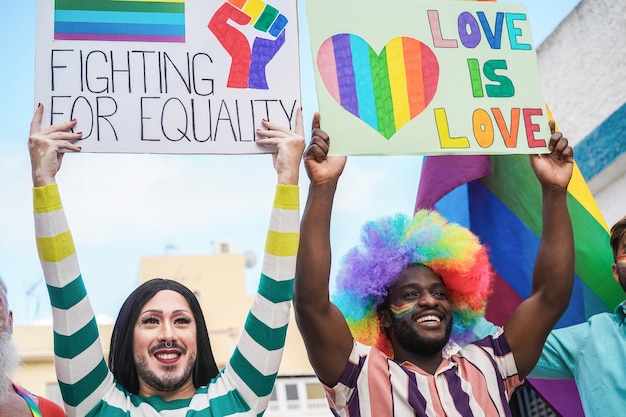 Multiracial gay people marching at LGBT pride parade with banners - Focus on drag queen