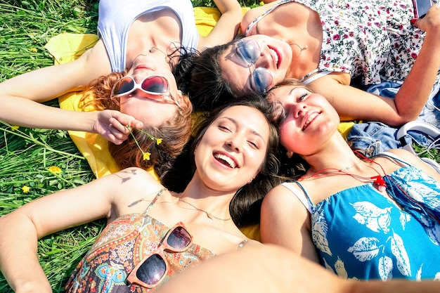 Multiracial girlfriends taking selfie at countryside picnic - Happy friendship concept and fun with young people and new technology trend - Sunny afternoon color tones - Framed hand holding smartphone