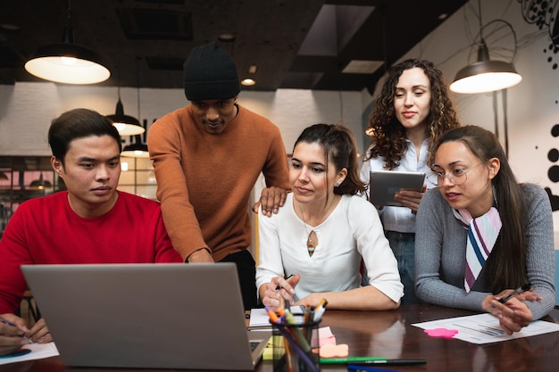 Multiracial group of five casual people looking at computer laptop discussing Coworking concept