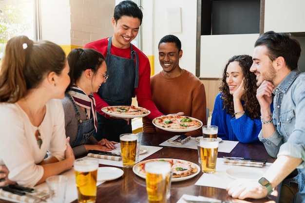 Multiracial group of friends in restaurant looking hungry the pizzas that the waiter is bringing