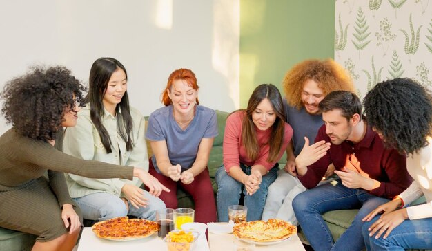 Photo multiracial group of happy friends eating pizza at home