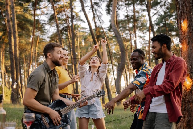 Multiracial group of people bearded hipster man playing guitar and friends dancing singing