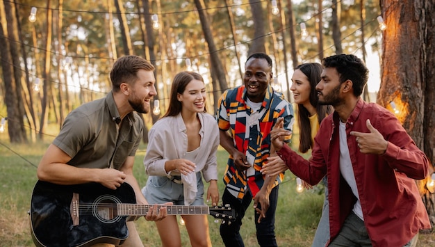 Multiracial group of people bearded hipster man playing guitar and friends dancing singing