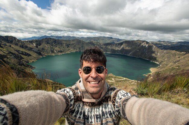 Photo multiracial hispanic young man taking a selfie in front of quilotoa lagoon in ecuador