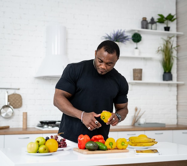 Multiracial man in kitchen ready to prepare meal with vegetables and fruits Guy is holding pepper Kitchen background Healthy food Vegans and vegetarians