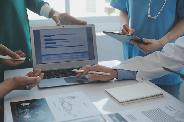 Multiracial medical team having a meeting with doctors in white lab coats and surgical scrubs seated at a table discussing a patients records