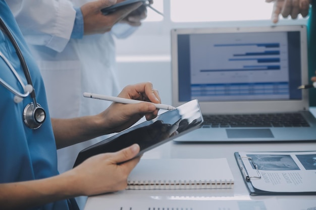 Multiracial medical team having a meeting with doctors in white lab coats and surgical scrubs seated at a table discussing a patients records