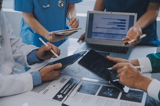 Multiracial medical team having a meeting with doctors in white lab coats and surgical scrubs seated at a table discussing a patients records