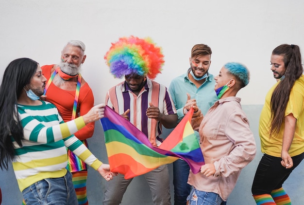 Multiracial people dancing at lgbt pride parade with rainbow flag while wearing safety mask under chin for coronavirus outbreak