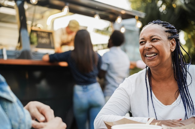 Multiracial people eating at food truck restaurant outdoor - Focus on african woman face