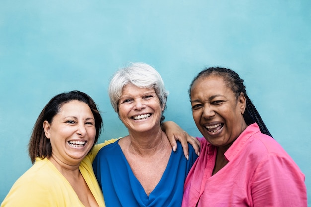 Multiracial senior women having fun hugging together outdoor - Focus on center woman face