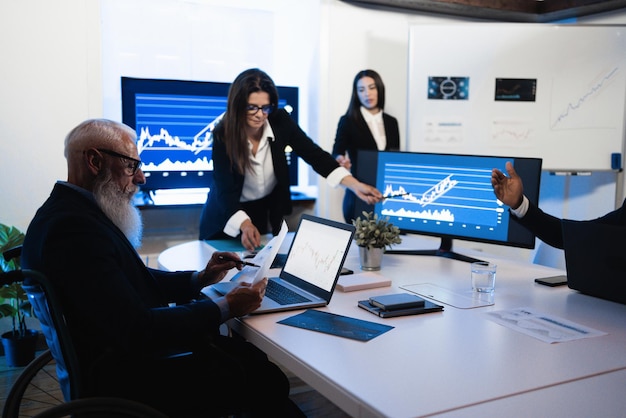 Multiracial trader team making stock market analysis conference inside hedge fund office  Soft focus on senior man face sitting in wheel chair