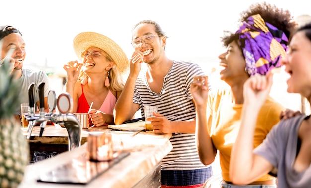 Multiracial trendy friends having fun drinking bear at sunset beach party