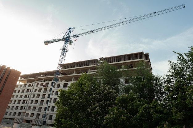 Multistorey residential building under construction and crane on a background of blue sky