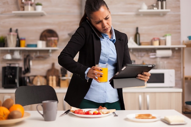 Multitasking woman talking on the phone, holding tablet and drinking a juice