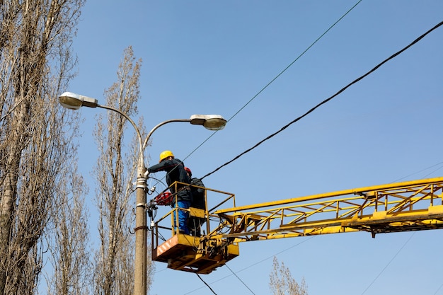 Municipal workers with helmets  and safety protective equipment installs wires on street lamp