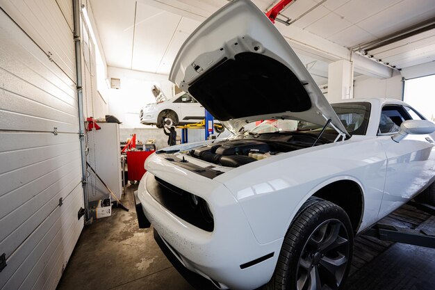 Muscle car with open hood at service repair station in lift